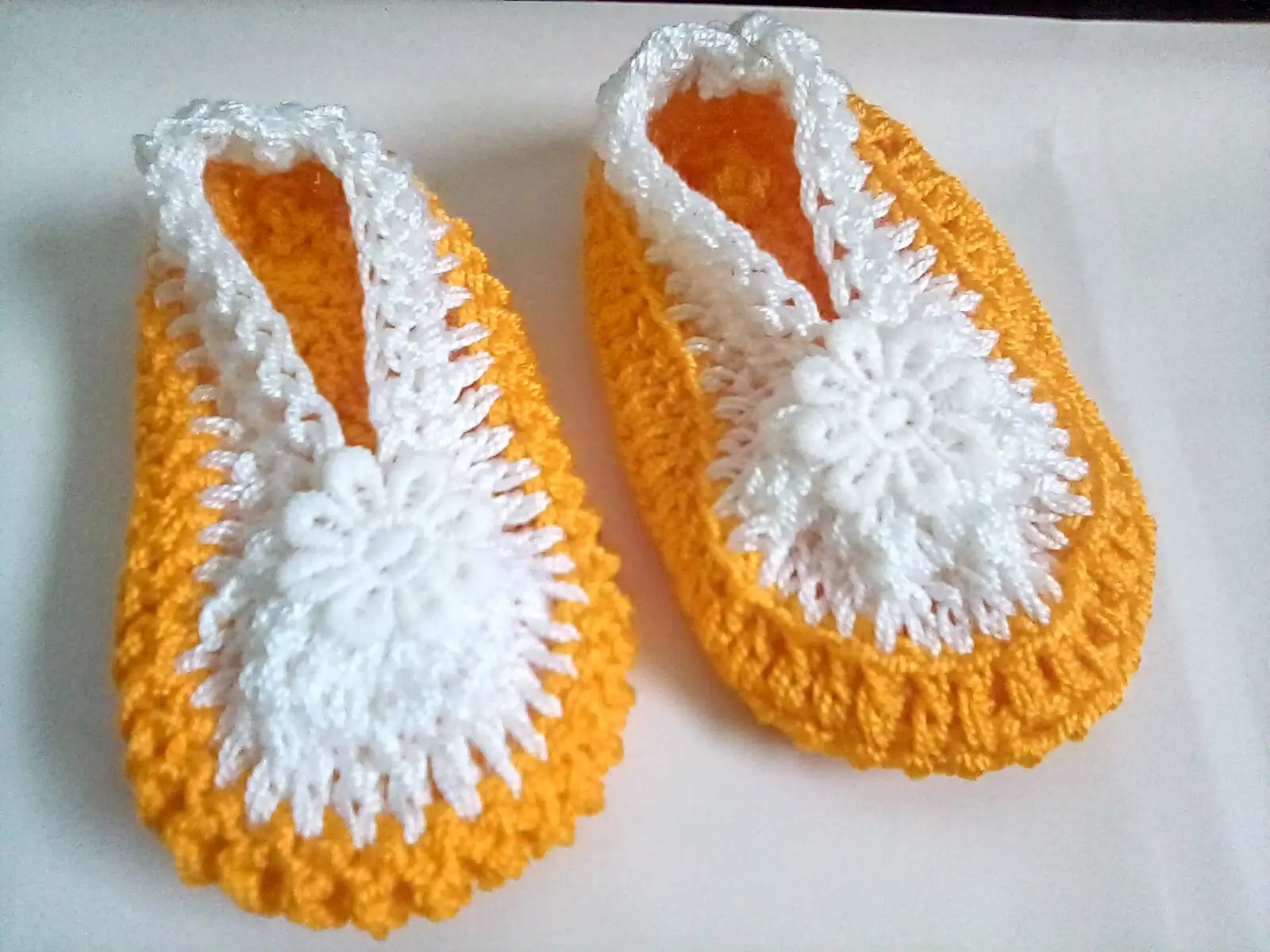 Zapatitos tejidos  a crochet, elaborados con hilo en tonos mostaza y blanco,